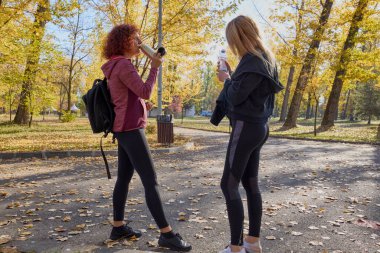 Orta yaşlı bir kadın arkadaşıyla parkta yürüyor, rahatlıyor, sohbet ediyor ve bir şeyler atıştırıyor..