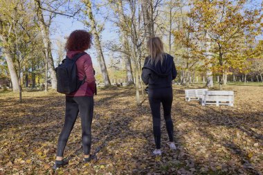 Orta yaşlı bir kadın arkadaşıyla parkta yürüyor, rahatlıyor, sohbet ediyor ve bir şeyler atıştırıyor..