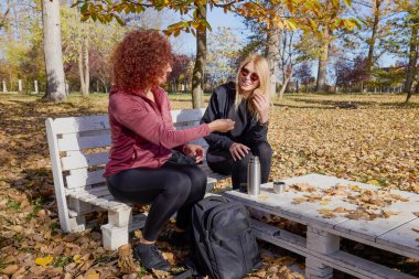 Orta yaşlı bir kadın arkadaşıyla parkta yürüyor, rahatlıyor, sohbet ediyor ve bir şeyler atıştırıyor..