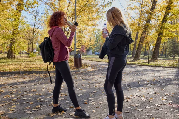 Orta yaşlı bir kadın arkadaşıyla parkta yürüyor, rahatlıyor, sohbet ediyor ve bir şeyler atıştırıyor..