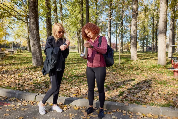 Orta yaşlı bir kadın arkadaşıyla parkta yürüyor, rahatlıyor, sohbet ediyor ve bir şeyler atıştırıyor..