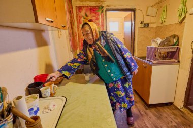 Mutfakta yaşlı bir köylü kadın bir masada otururken kahve yapıp içiyor..