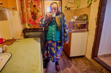 Mutfakta yaşlı bir köylü kadın bir masada otururken kahve yapıp içiyor..