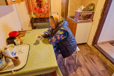 Mutfakta yaşlı bir köylü kadın bir masada otururken kahve yapıp içiyor..