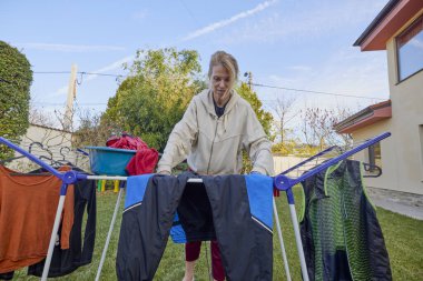 Bahçedeki kadın kurutucuya kurutmak için çamaşır asıyor.