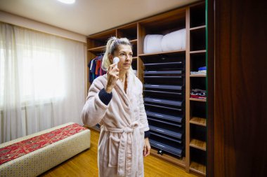 Evde orta yaşlı bir kadın sabahları makyaj yapıyor.