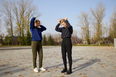 İki orta yaşlı kadın bir sonbahar sabahı parkta ısınma egzersizi yapıyor.