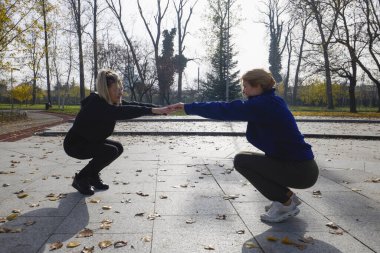 İki orta yaşlı kadın bir sonbahar sabahı parkta ısınma egzersizi yapıyor.