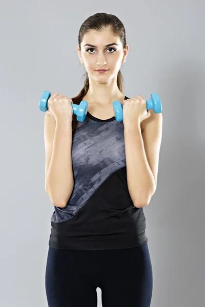 Mulher esportiva fazer seu treino com halteres, isolado em bac cinza — Fotografia de Stock