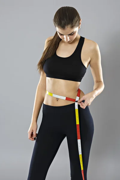 Uma jovem mulher medindo sua cintura isolada em fundo cinza — Fotografia de Stock