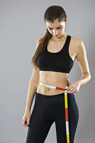 A young woman measuring her waist isolated on gray background — Stock Photo, Image