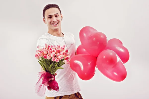 Jonge man geeft tulpen en hartvormige ballonnen — Stockfoto