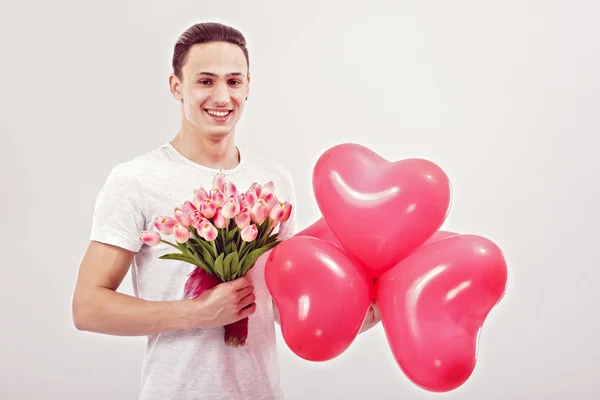 Jeune homme donne des tulipes et des ballons en forme de coeur — Photo