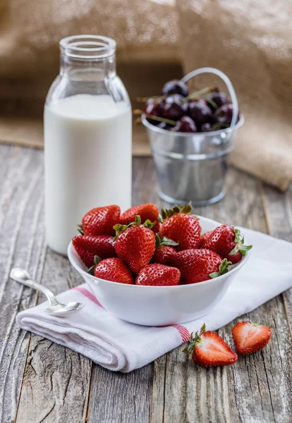 Fresas en un tazón con una botella de leche — Foto de Stock