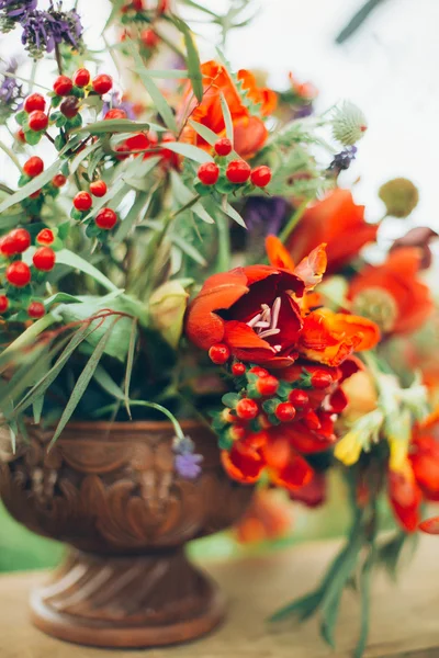 beautiful wild red flowers are metal in a bronze vase on the chest outdoors on a grass background