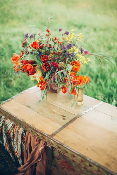 Beautiful wild red flowers are metal in a bronze vase on the chest outdoors on a grass background — Stock Photo, Image