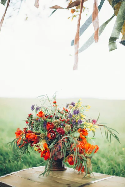 Beautiful wild red flowers are metal in a bronze vase on the chest outdoors on a grass background — Stock Photo, Image