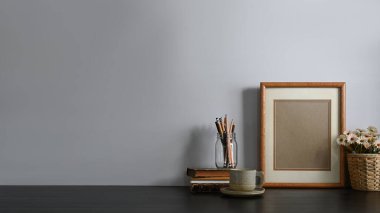 Çalışma alanı kalem tutacağı, kitap yığını, resim çerçevesi, kahve fincanı ve saksı çiçeğinin arka planda oturma odası olan rahat çalışma masasında bir araya getirilmesi. Düzenli çalışma alanı kavramı.