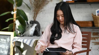 Genç yaratıcı tasarımcı modern kafede otururken dijital tablete kalem çizimi yapıyor..