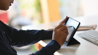 Modern çalışma masası arkaplanı üzerinde beyaz ekran tabletine yazı yazan genç ve şık yapımcının yan görüntüsü..