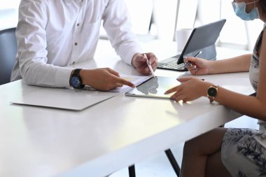 Dijital tablet kullanan ve modern ofiste yeni bir proje üzerinde çalışan koruyucu maskeli iki iş adamı..