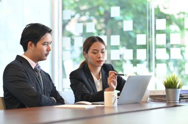 Kendine güvenen iş kadını, modern ofisteki toplantı odasında otururken yanındaki meslektaşına yeni bir projeyi anlatıyor..