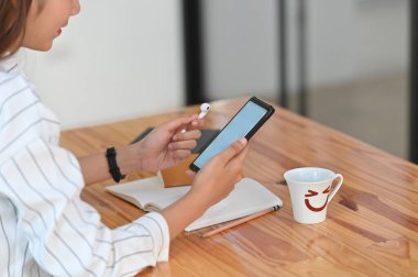 Çizgili tişörtlü güzel bir kadının elinde beyaz ekran akıllı telefon ve kablosuz kulaklıkla modern ahşap masada arka plan olarak rahat bir oturma odasında otururken görüntüsü..
