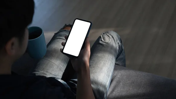 年轻人坐在沙发上 一边用智能手机一边举杯咖啡的后视镜 — 图库照片