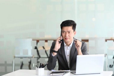 İş adamı ofisinde otururken cep telefonuyla konuşuyor..