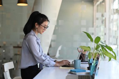 Tablet bilgisayarda çalışan ve rahat bir iş yerinde oturan kendine güvenen bir iş kadınının yan görüntüsü.