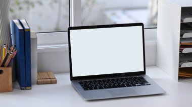 Boş ekran, kitaplar ve ofis malzemelerini beyaz ofis masasına dizüstü bilgisayarla yapıştır.