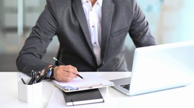 Dizüstü bilgisayarla çalışan ve ofis masasındaki mali raporları analiz eden işadamının görüntüsü..