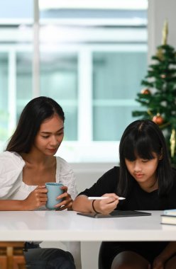 Evdeki tablette kızının çalışmasına yardım eden annenin portresi..