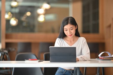 Modern oturma odası arka planda olan rahat çalışma masasında bilgisayar tableti ile internette sörf yapan muhteşem genç bir kadın..