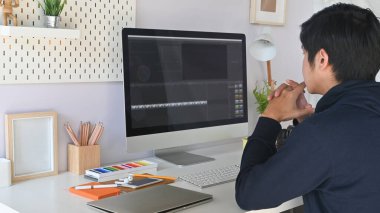 Çalışma masasında video düzenleyici programı kullanırken, delikanlının arkasından kırpılmış görüntü.