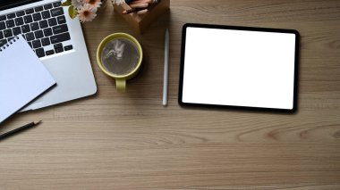 Dijital tablet, laptop ve kahve fincanı ahşap masada. Metin veya reklam içeriğiniz için boş ekran.