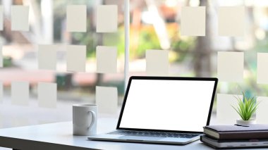 Bilgisayarın beyaz ekranlı fotoğrafı, saksı bitkisi, kahve fincanı ve kitap yığını bulanık arkaplanlı modern çalışma masasında bir araya getiriliyor..
