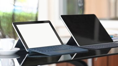 Boş ekranda klavye çantası olan iki tablet bilgisayar ve cam masaya koyulan boş ekran.