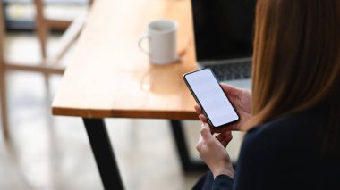 Proje yöneticisi olarak çalışan çekici bir kadının, ahşap çalışma masasında otururken beyaz ekranlı kesilmiş siyah akıllı telefonu kullanması / tutması..