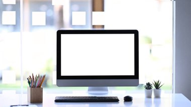 Modern bilgisayarın, kırtasiyenin ve bitkinin ön görüntüsü beyaz masada. Reklam metni için beyaz boş ekran.