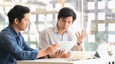 İş planlarından bahseden / tartışan / planlayan genç iş geliştirme ekibinin fotoğrafı arka planda rahat bir ofisi olan modern toplantı masasında otururken.