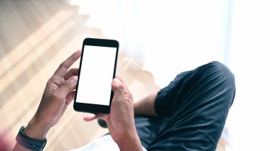 Oturma odasında bacak bacak bacak üstüne atmış ve akıllı telefon kullanan genç adamın yakın görüntüsü..