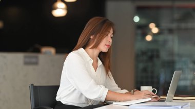 Genç bir kadının çalışma masasında dizüstü bilgisayar kullanırken çekilmiş bir fotoğrafı..