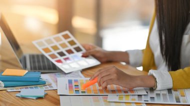 Ahşap çalışma masasında otururken güzel tasarımcının renk rehberinden rengini seçerken yan görüntüsü.