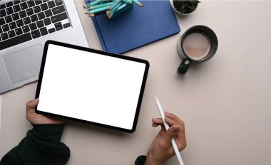 Kadın tasarımcı elinin boş ekranlı dijital tableti tutuşu ve çalışma alanında stil kaleminin üst görüntüsü.