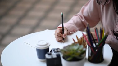 Kalem tutan kadın ressamın şık atölyesinde eskiz defterine çizim yaptığı yakın plan..