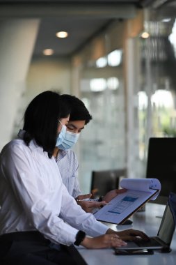 Koruyucu maske ve muhasebe sürecinde bilgi tartışması yapan iki finans uzmanı.