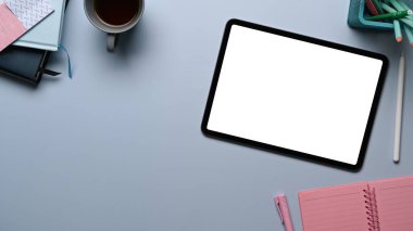 Boş ekran, not defteri, kahve fincanı ve yaratıcı tasarımcı işyerindeki gri masanın üzerindeki bitkiyle dijital tabletin üst görünümü.