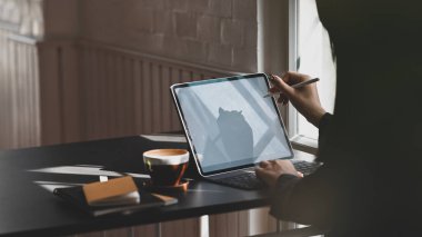 Genç yönetici, arka plan olarak lüks ofis odası olan modern çalışma masasında çalışmayı düşünürken bilgisayarın tabletine elektrikli kalem doğrultuyor..