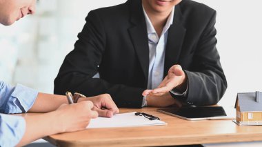 Emlakçı, modern ahşap masada mavi gömlekli akıllı bir adama ev sigortası ya da ev sahipliği teklif ediyor. Anlaşma imzalanırken, Komisyoncu / Satıcı kavramı.